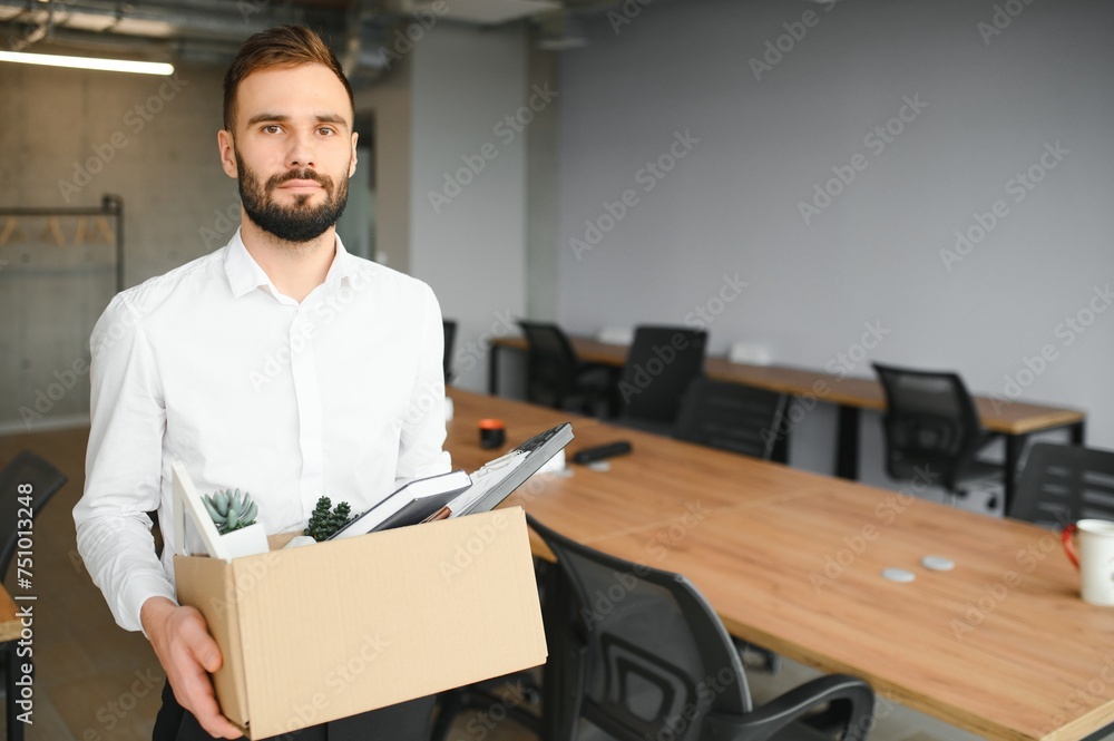 Young handsome businessman in light modern office with carton box. Last day at work. Upset office worker is fired Young handsome businessman in light modern office with carton box. Last day at work. Upset office worker is fired