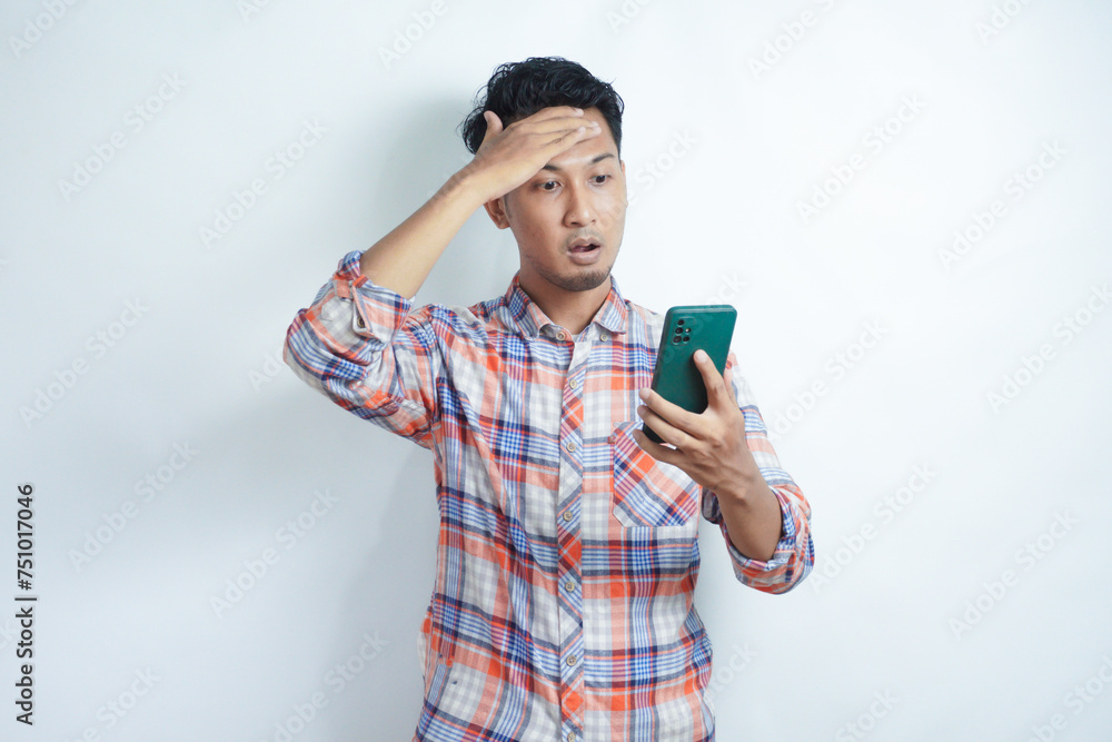 Adult Asian man looking to his mobile phone with wow expression Adult Asian man looking to his mobile phone with wow expression
