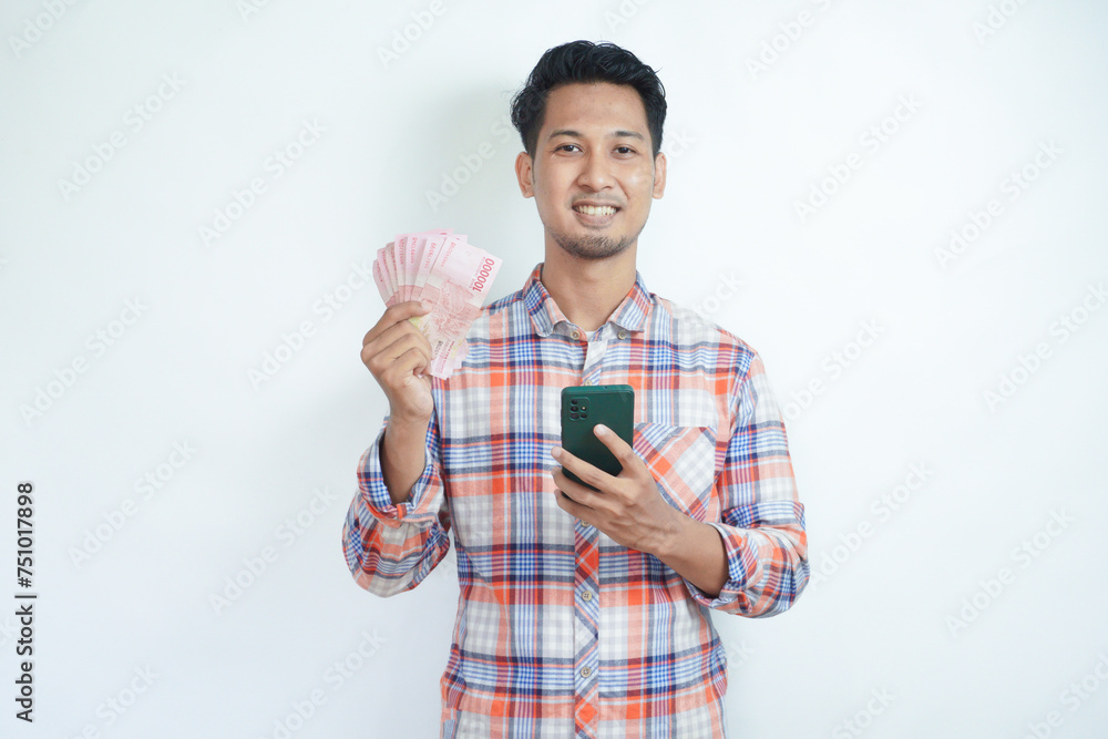 Adult Asian man holding money and mobile phone smiling happy at the camera Adult Asian man holding money and mobile phone smiling happy at the camera