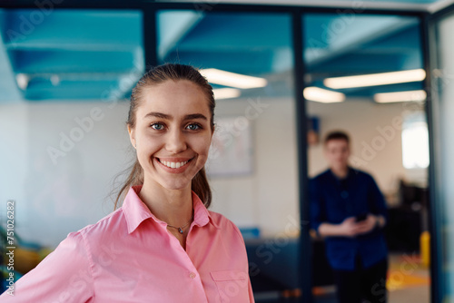 Portrait of young smiling business woman in creative open space coworking startup office. Successful businesswoman standing in office with copyspace. Coworkers working in background
