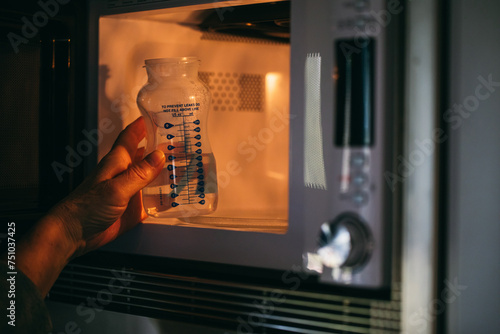 Woman taking baby bottle with water from microwave  photo