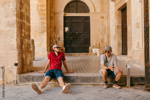 Two men with sunglasses and cap resting on a city step. photo