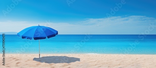 A vibrant blue umbrella casting shade on the sandy beach, with the sparkling blue ocean in the background.
