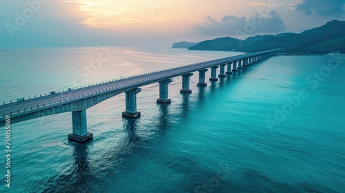Aerial view of a long bridge crossing a tranquil blue sea at dawn © Vodkaz