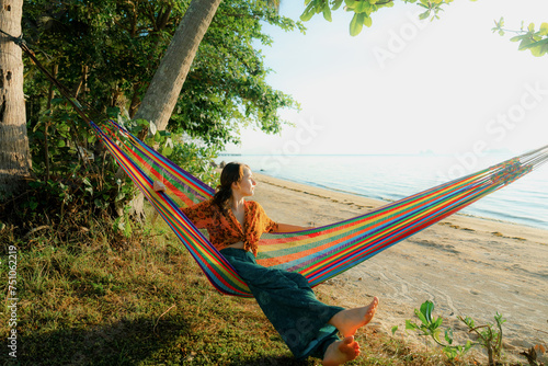 Woman laying on rainbow color hammock on the beach