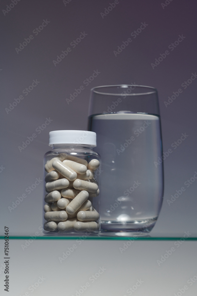 A bottle with pill capsules and a glass of water on a gray background A bottle with pill capsules and a glass of water on a gray background