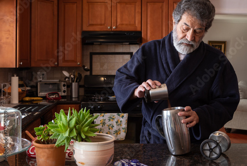 Retired latin man using a french press making coffee in his kitchen photo