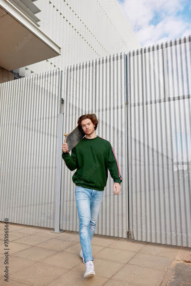 Active young guy walking with skateboard near building Active young guy walking with skateboard near building