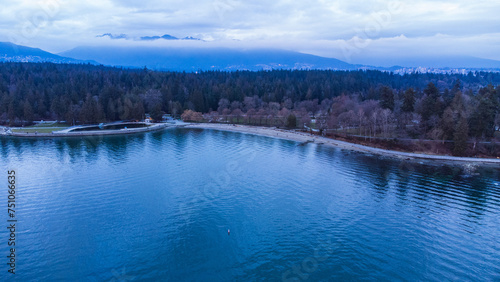 Stanley Park Seawall. Clouds reflect off a calm ocean. North Shore mountains in the background. 