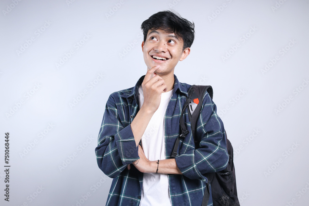 Asian young boy wear backpack, touching his chin and looking up with smile, thinking of something Asian young boy wear backpack, touching his chin and looking up with smile, thinking of something