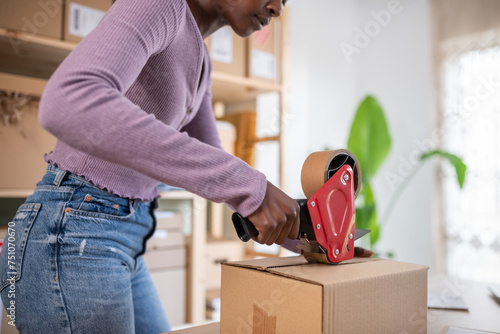 Black employee sealing carton box in office photo