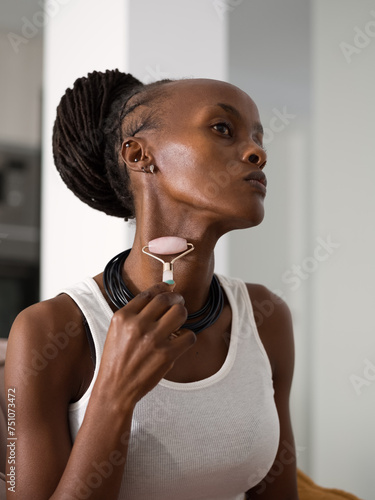 Black woman smoothing neck skin with roller photo