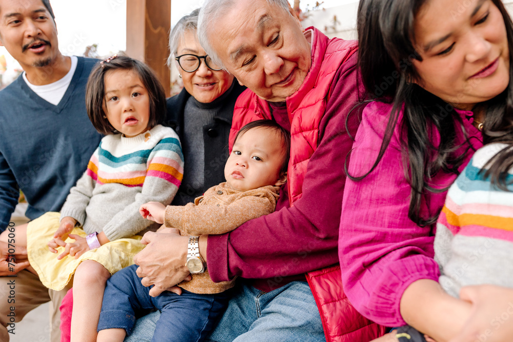 Asian family with grandparents sitting outdoors together Asian family with grandparents sitting outdoors together