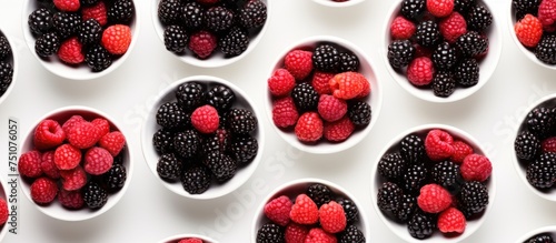 A ceramic white bowl is filled with a mixture of red and black raspberries, illuminated by modern lighting, against a plain white background. The view is from above.