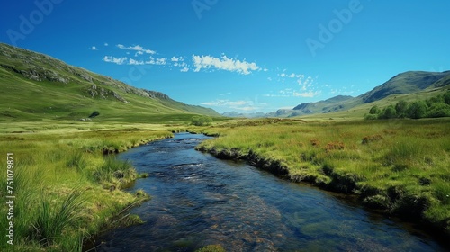 A peaceful stream winding through a mountainous landscape, with a cloudless blue sky as a backdrop.