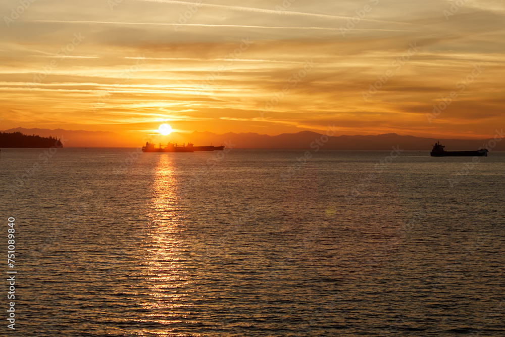Sun setting down over the sea with cargo ships silhouettes in its light.