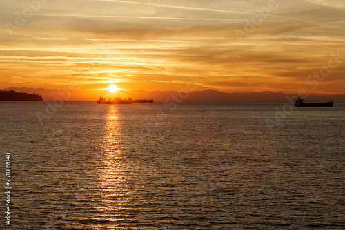 Sun setting down over the sea with cargo ships silhouettes in its light.