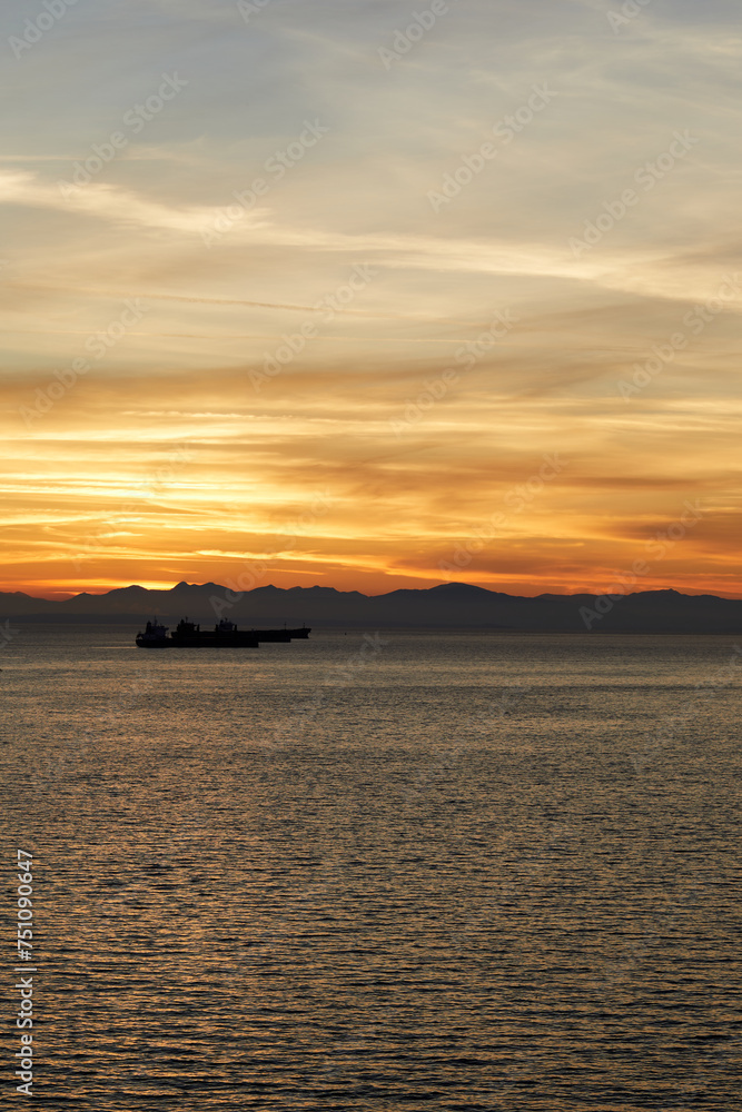 3 cargo ships lined up next to each other on a sea at dusk.