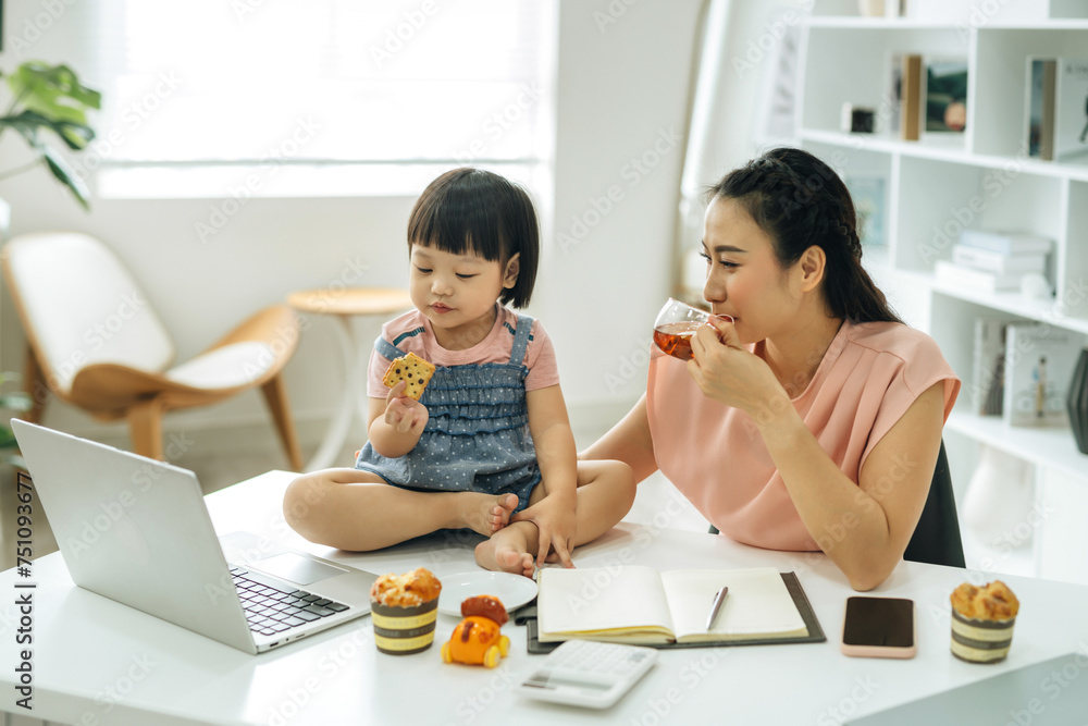 young woman with her little daughter is using a laptop at home office young woman with her little daughter is using a laptop at home office