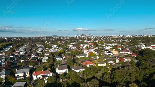 Grey Lynn And Ponsonby Suburb with buildings and homes at sunset. Sky Tower with skyline of Auckland City in background. Dense green forest trees on road in New Zealand. Aerial backwards wide shot.