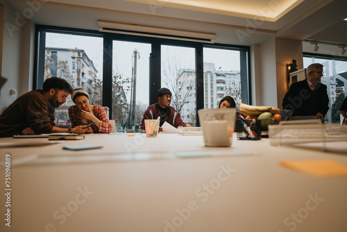 A group of diverse professionals is engaged in a business meeting in a well-lit office with expansive windows and modern decor.