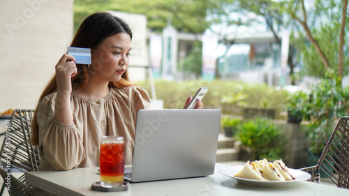 Young beautiful asian woman using using laptop and holding credit card with shocked or surprised face emotion in coffee shop cafe