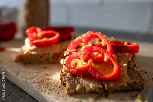 An open-faced sandwich with hummus and red pepper on a wooden board.