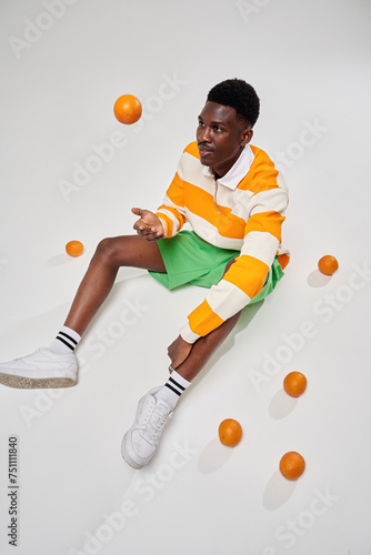 A black man sits on a pou with oranges photo