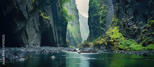 A small river winds through a narrow gorge, surrounded by vibrant green foliage in a lush canyon setting.