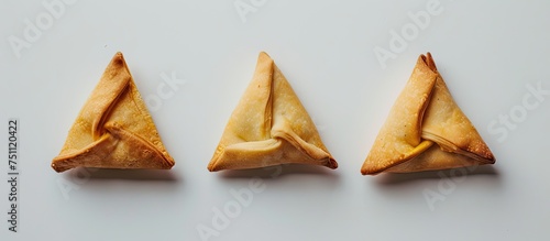 Three pieces of Hamantashen, traditional Jewish pastries for Purim, are creatively shaped like triangles and displayed on a blank backdrop.