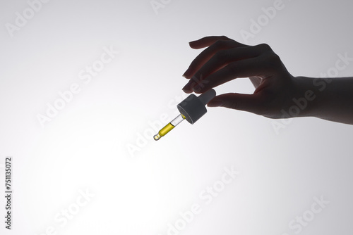 Hand of woman with pipette drop of serum or hyaluronic acid on gray ba