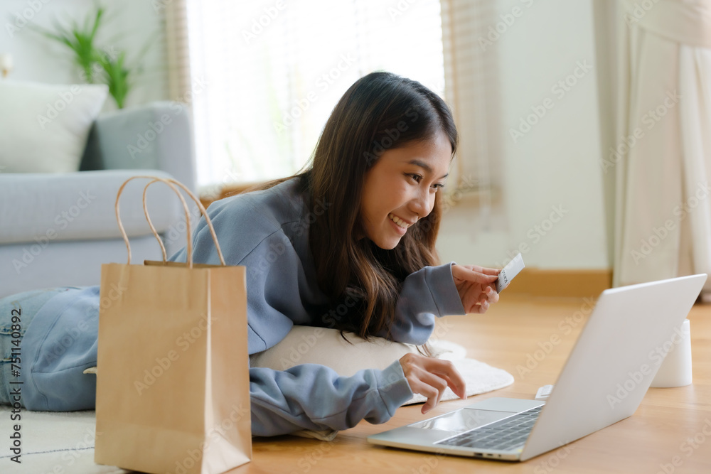 Young asian happy woman smile in living room at home, Using computer laptop, lying on the floor at house, online banking payment through the internet from bank card. Shopping online with credit card Young asian happy woman smile in living room at home, Using computer laptop, lying on the floor at house, online banking payment through the internet from bank card. Shopping online with credit card