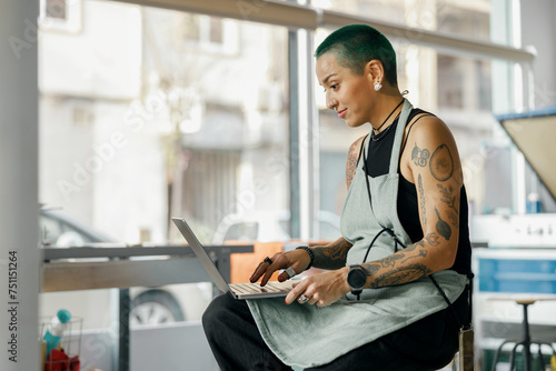 Positive female designer sitting with laptop on background of print machine in workshop