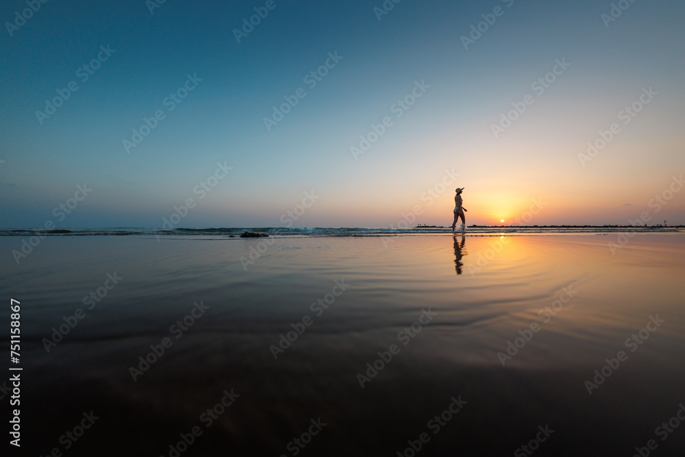 silhouette of a woman walking along the seashore. Spiritual Peace Meditation. A happy girl walks along the seashore against the backdrop of sunset.
