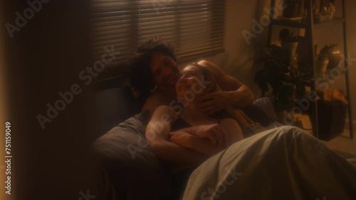 Young loving man and woman cuddling in bedroom, chatting and smiling in evening at home