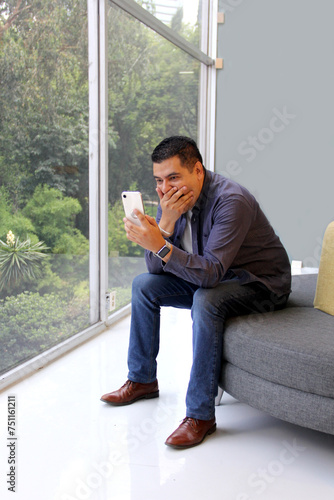 40-year-old dark-skinned Latino man in his office uses his cell phone to work, make payments, video calls and find discounts and promotions © Arlette