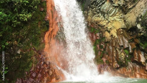 The famous waterfall in Pulangbato Valencia. The water falls down in a nice pool where there are big rocks. The water in the pool looks green and the sand and rocks are red. photo