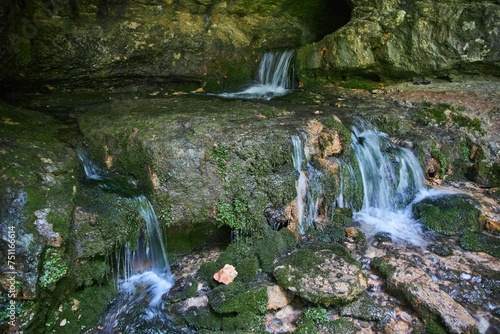 Wild cave outside. The river flows out of the cave  a waterfall. Speleology and surveys