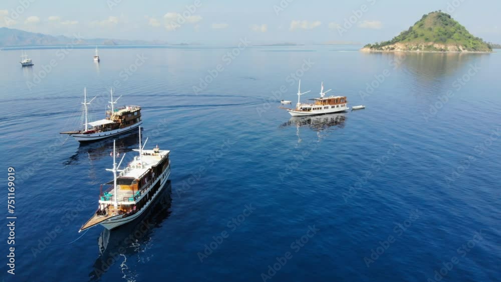 A group of three small cruise ships floating on calm waters near Pulau Kelor island, close to Komodo Park, showcasing the tranquil beauty of Indonesia and Asia A group of three small cruise ships floating on calm waters near Pulau Kelor island, close to Komodo Park, showcasing the tranquil beauty of Indonesia and Asia