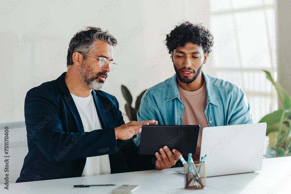 Two professional men collaborating in modern office using tablet and laptop Two professional men collaborating in modern office using tablet and laptop