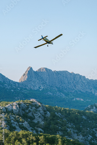 A small yellow firefighting plane flies over the mountains 