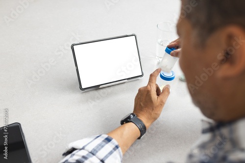 A senior man is looking at a tablet with a blank screen, providing copy space, while holding a glass