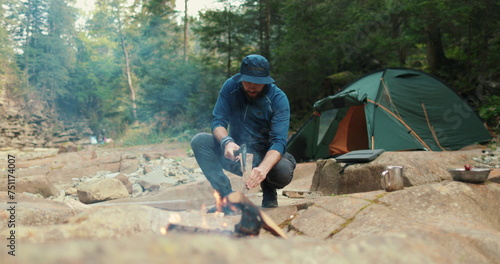 a male tourist chops firewood with a small ax near a campfire in the forest. the traveler prepares wood for the fire. man in the wild. outdoor hiker, wilderness survival, campfire