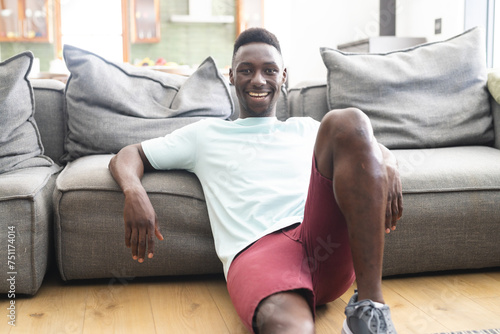 Young African American man with a bright smile sits relaxed on a grey sofa
