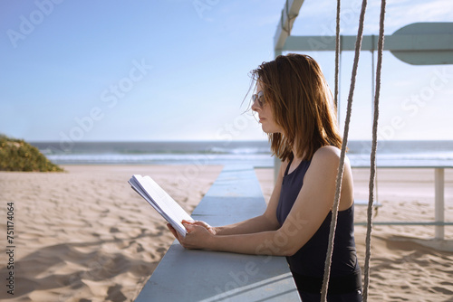 A young woman on the ocean reading a book photo
