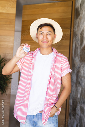 An Asian man holding a 'vote' badge proudly displays it