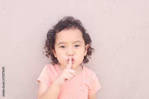 Portrait of cute toddler keeps index finger over his lips.