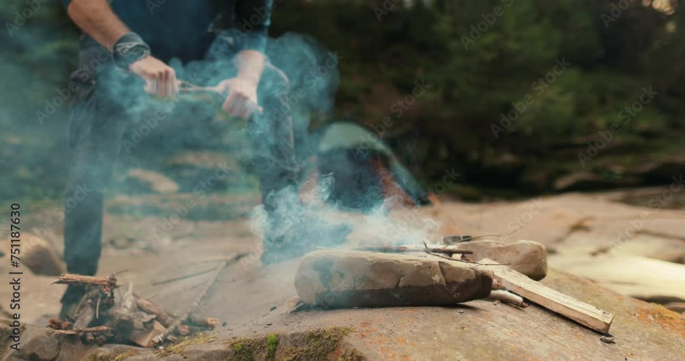 a male tourist chops firewood with a small ax near a campfire in the forest. the traveler prepares wood for the fire. man in the wild. outdoor hiker, wilderness survival, campfire a male tourist chops firewood with a small ax near a campfire in the forest. the traveler prepares wood for the fire. man in the wild. outdoor hiker, wilderness survival, campfire