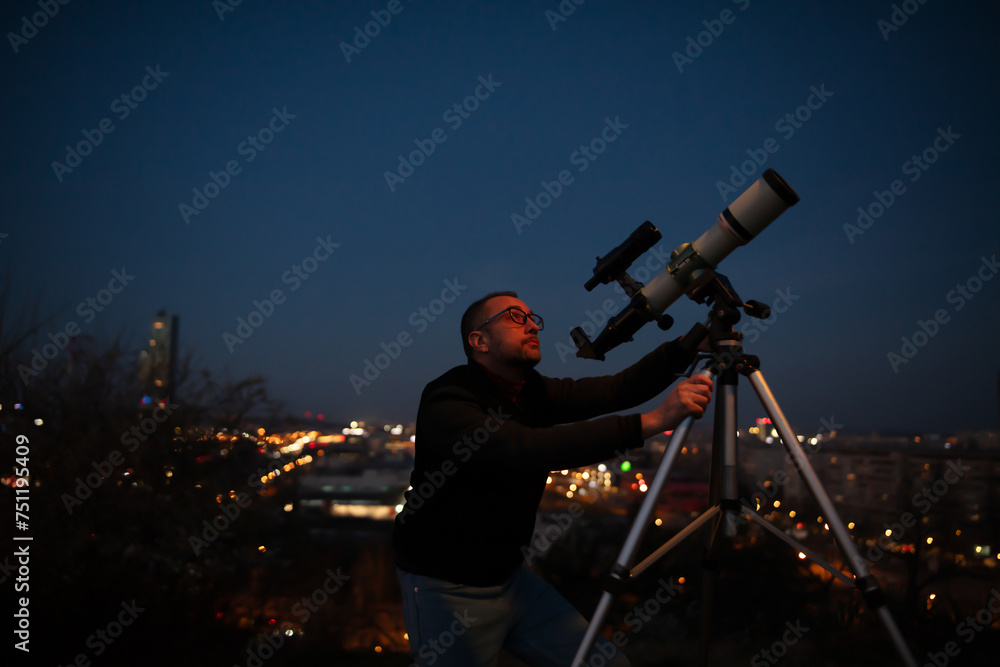Amateur astronomer looking at the evening skies, observing planets, stars, Moon and other celestial objects with a telescope in urban city area.