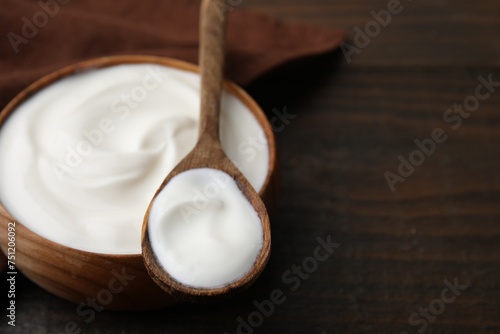 Delicious natural yogurt in bowl and spoon on wooden table, closeup. Space for text